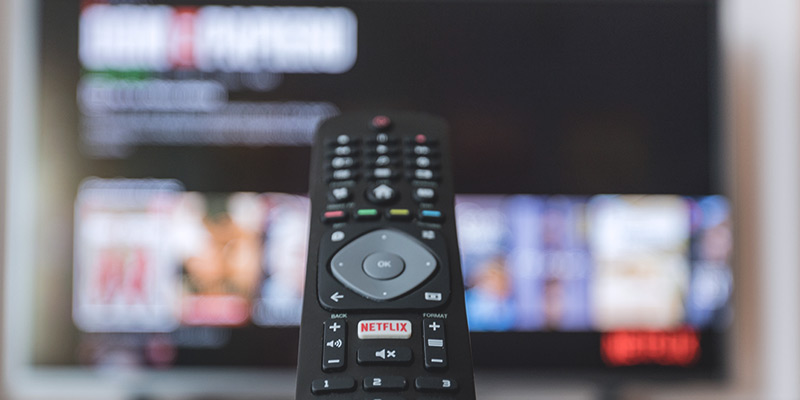 Strom sparen beim TV: Bild einer Fernbedienung mit Fernseher im Hintergrund