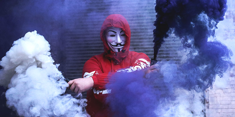 Hacker Anonymous: Mann mit Guy-Fawkes-Maske und Petarden